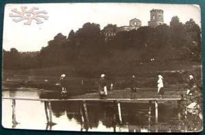 Жінки йдуть через кладку на річці Корчик на фоні корецького замку. Стара фотографія.